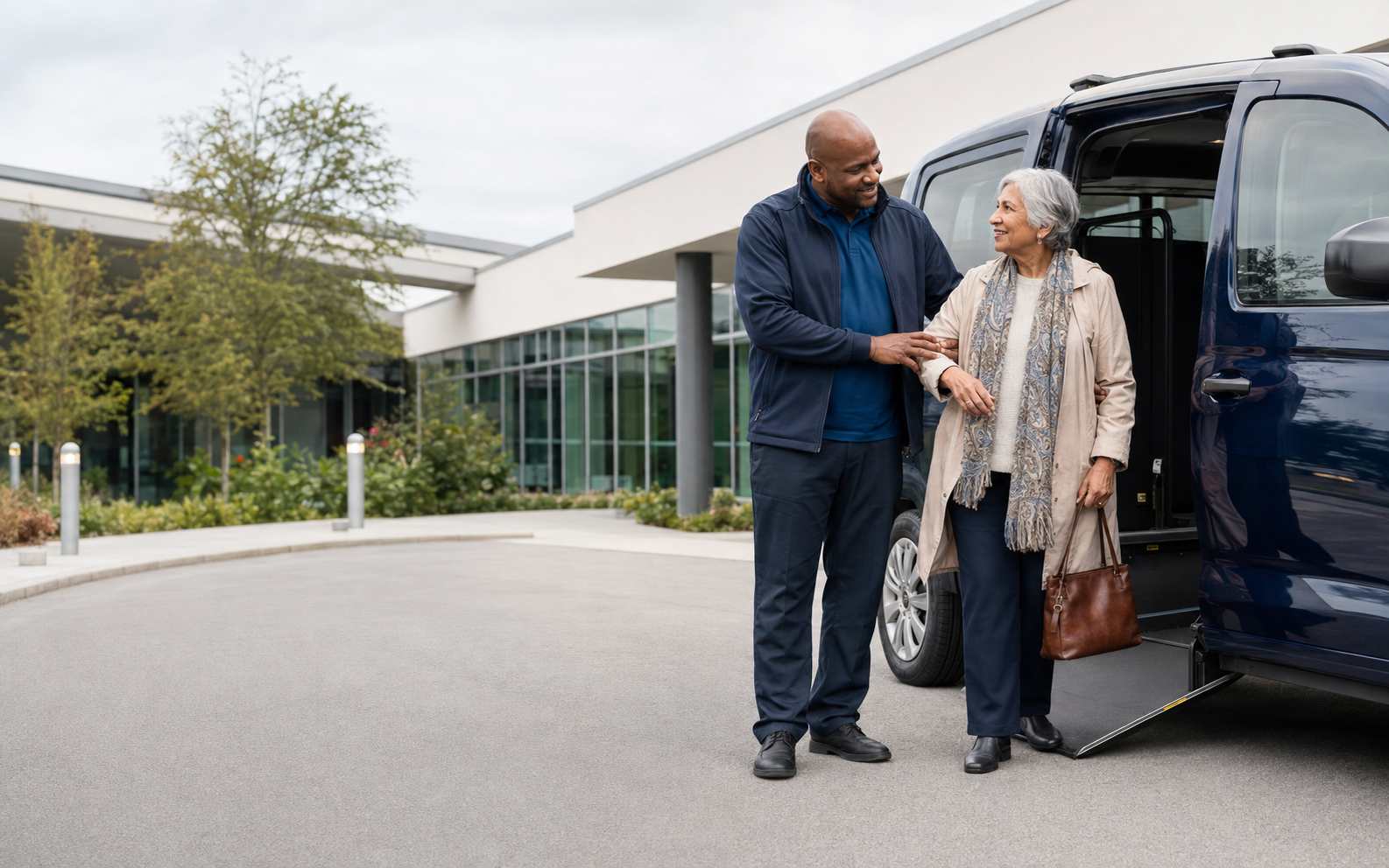 A patient transport professional reassuring an older passenger beside an accessible vehicle